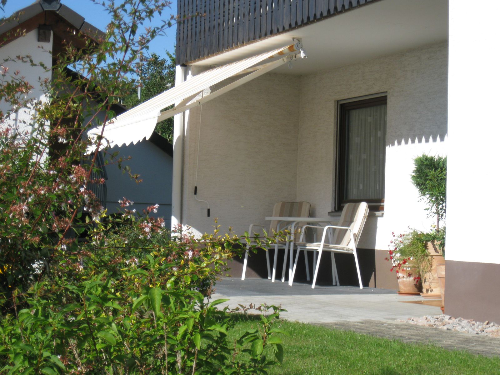 Überdachte Terrasse mit Markise, Tisch und Stühlen am Haus