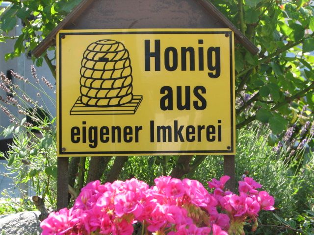 Schild „Honig aus eigener Imkerei“ zwischen blühenden Blumen